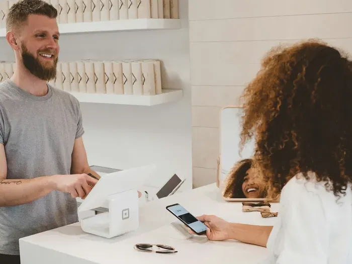 Smiling cashier assisting customer making a mobile payment at modern retail store counter